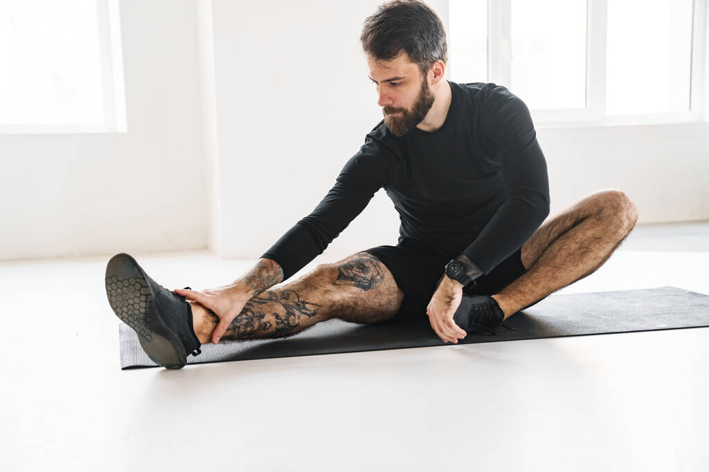 Bearded sportsman with tattoo doing exercise while working out indoors - Photo, Image