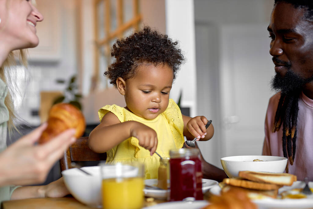 Schöne multiethnische Familie mit Kind frühstückt zu Hause in heller, gemütlicher Küche. - Foto, Bild