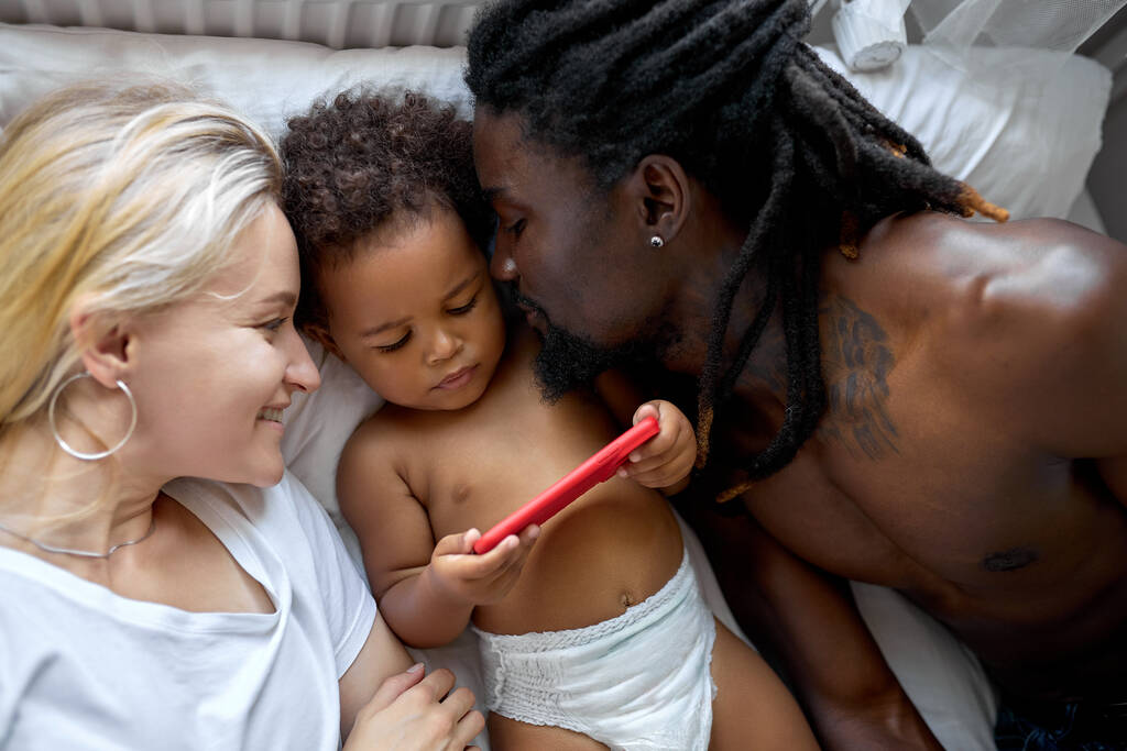 αξιολάτρευτο μαύρο παιδί κόρη έχουν τη διασκέδαση με τους γονείς βλέποντας βίντεο στο smartphone - Φωτογραφία, εικόνα