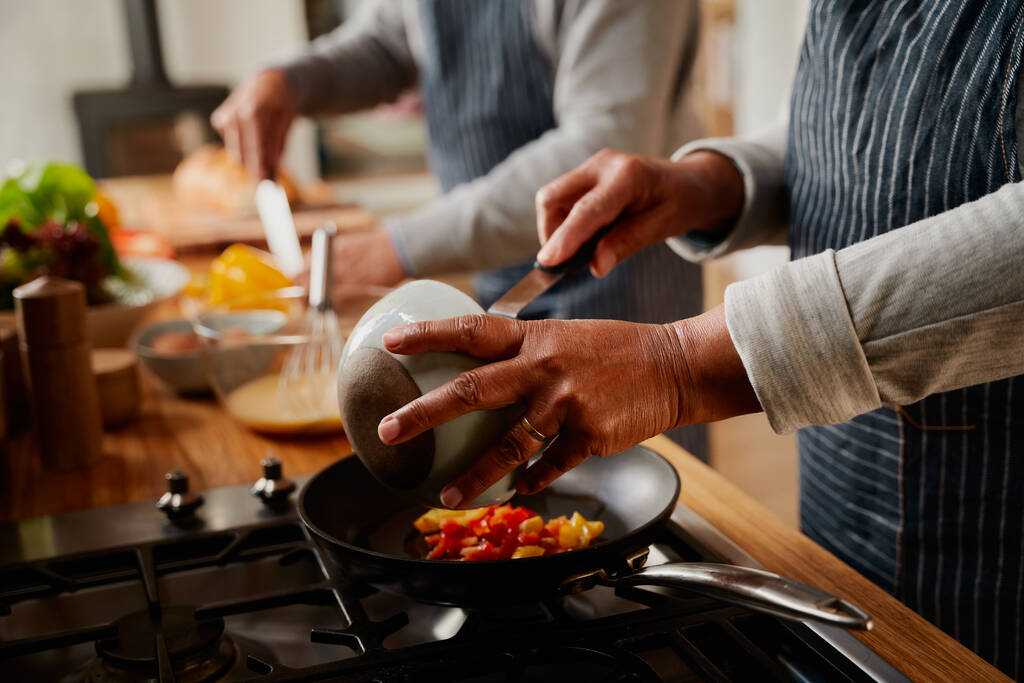 多文化の高齢者のカップルの手ストーブで現代的なキッチンで一緒に健康的な朝食を調理. - 写真・画像