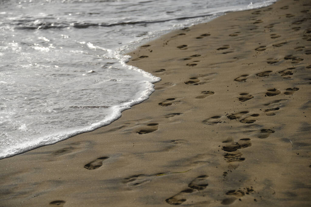 Une belle vue sur le sable sur la plage avec des vagues mousseuses et des empreintes de pas - Photo, image