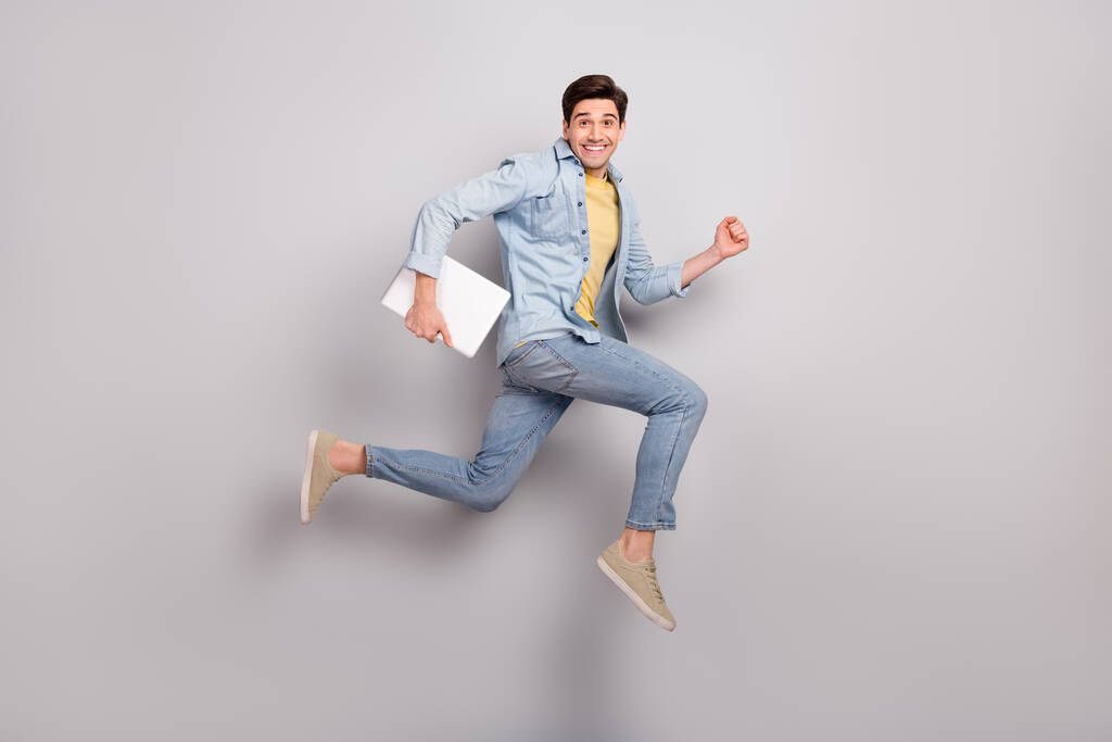 Foto von attraktiven lustigen Kerl gekleidet Jeanshemd Halter Gerät springen hohe isolierte graue Farbe Hintergrund - Foto, Bild