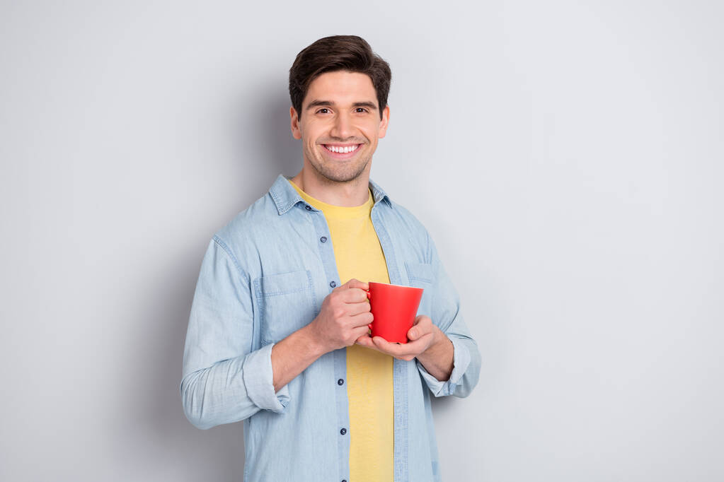 Photo of cheerful attractive guy dressed denim shirt enjoying hot coffee isolated grey color background - Foto, immagini