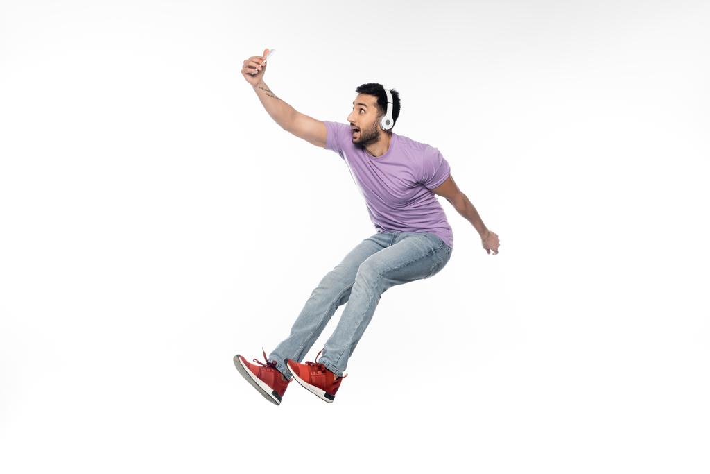 allegro uomo in cuffie wireless prendere selfie e levitare sul bianco - Foto, immagini