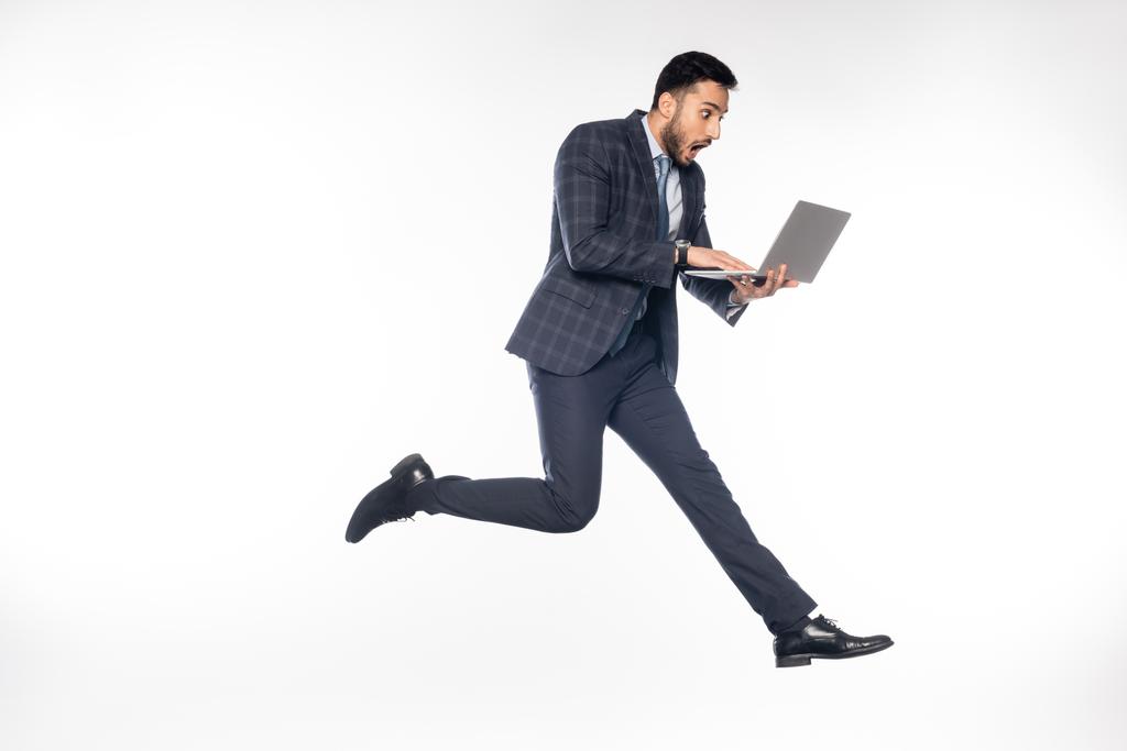 шокований бізнесмен у костюмі стрибає, використовуючи ноутбук на білому
  - Фото, зображення