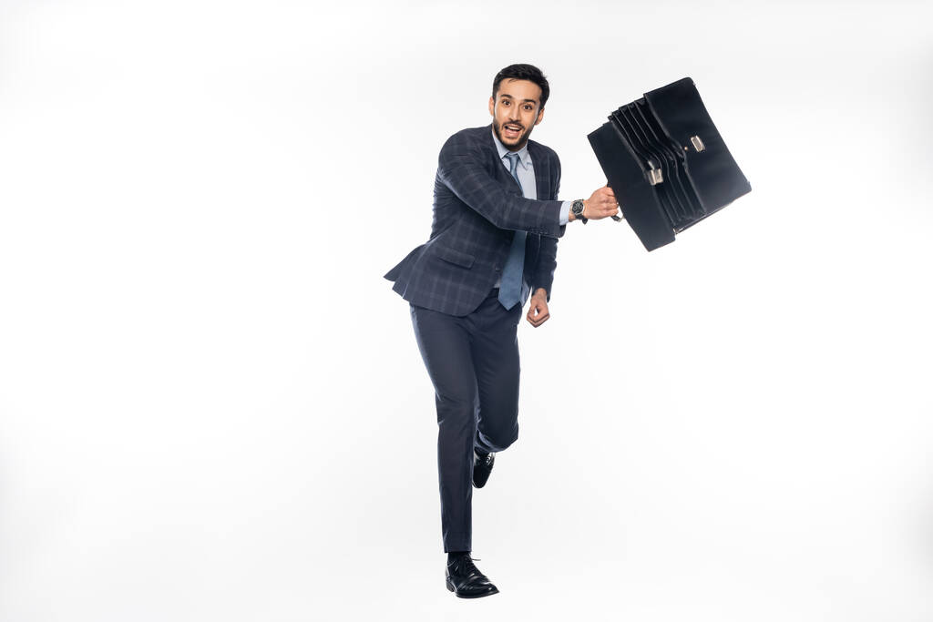 счастливый бизнесмен в костюме прыгает с портфелем на белом  - Фото, изображение
