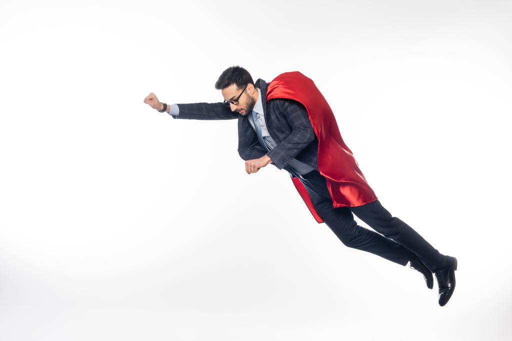 hombre de negocios con traje, gafas y capa de superhéroe levitando sobre blanco  - Foto, Imagen