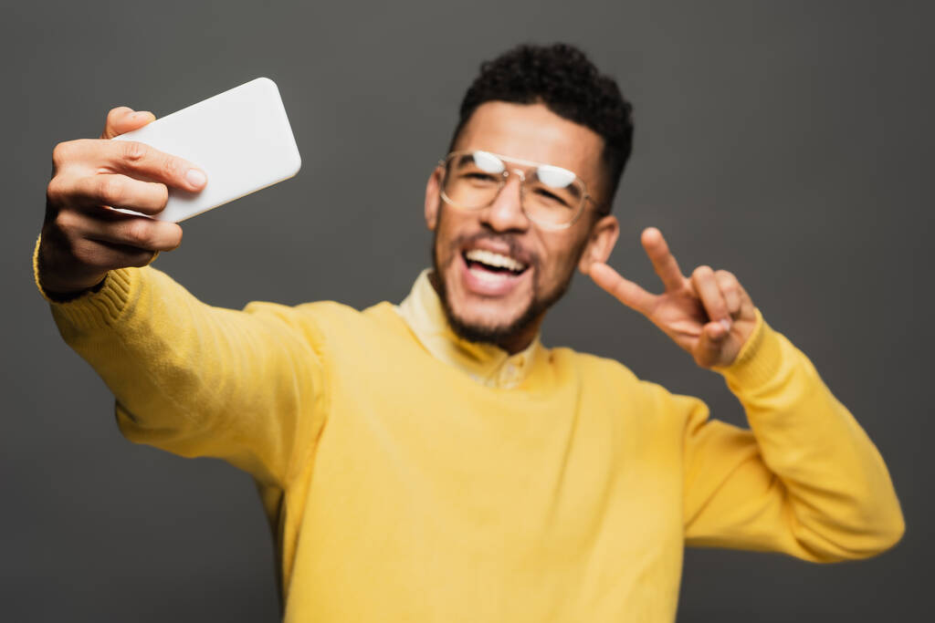 wazig opgewonden Afrikaans amerikaanse man in bril het nemen van selfie geïsoleerd op grijs - Foto, afbeelding