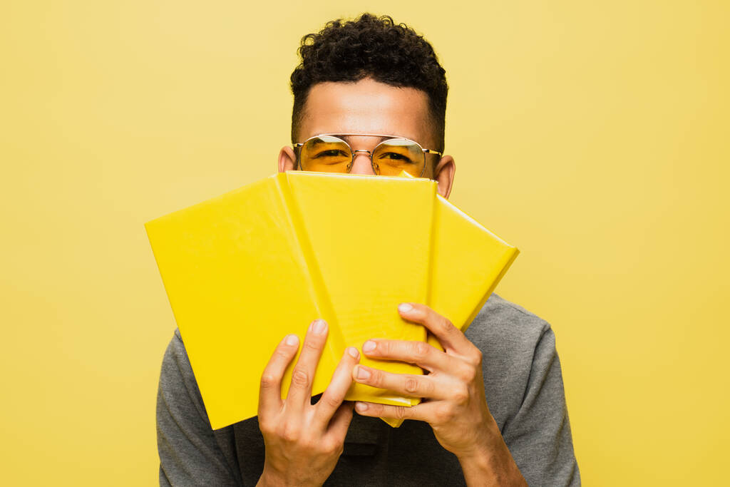 afro-amerikai férfi napszemüveg borító arc könyvek elszigetelt sárga  - Fotó, kép