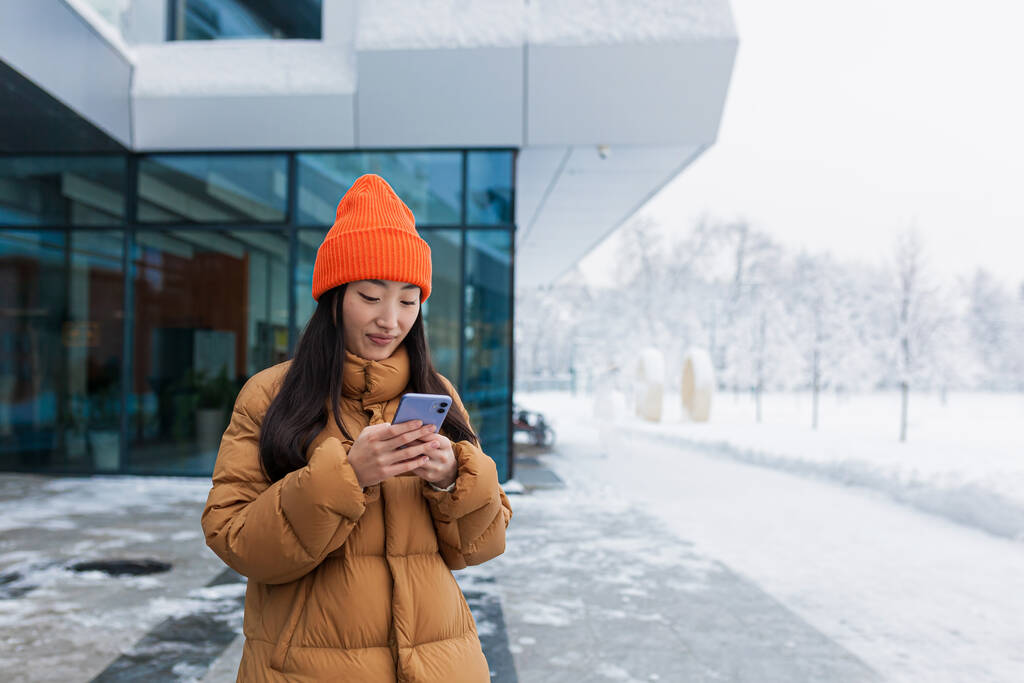 Портрет азиатской девушки, студентки, гуляющей и пользующейся телефоном в снежный зимний день - Фото, изображение