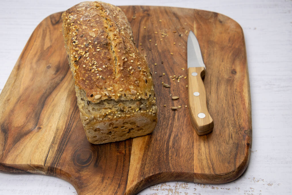 hausgemachtes Brot mit Samen und Messer auf Holzbrett - Foto, Bild