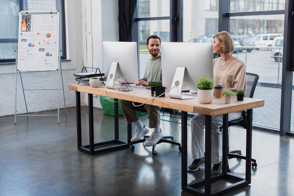 задоволені міжрасові колеги дивляться один на одного під час роботи в сучасному офісі
 - Фото, зображення