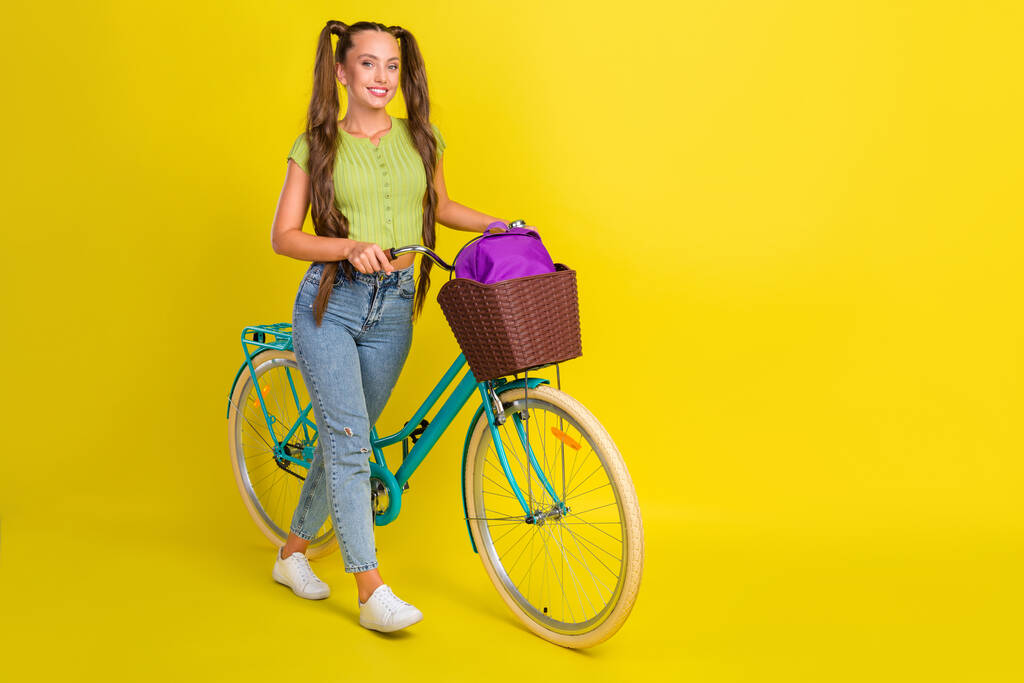 Ganzkörpergröße Ansicht von attraktiven fröhlichen Mädchen zu Fuß Fahrrad verbringen Urlaub isoliert über helle gelbe Farbe Hintergrund - Foto, Bild
