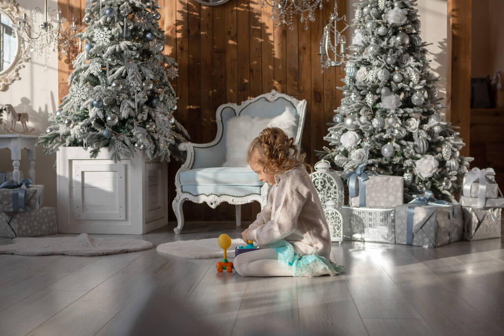 Uma menina está brincando no chão contra o fundo das árvores de Natal - Foto, Imagem