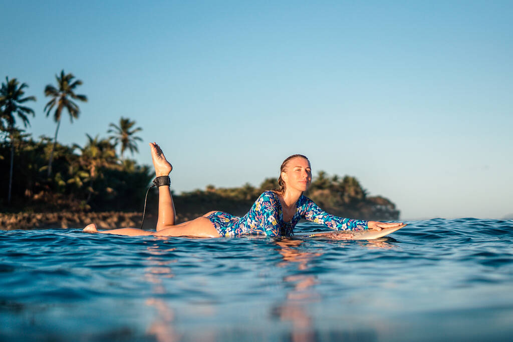 Porträt eines blonden Surfermädchens auf einem weißen Surfbrett im blauen Ozean vom Wasser aus am Strand von Encuentro in der Dominikanischen Republik - Foto, Bild