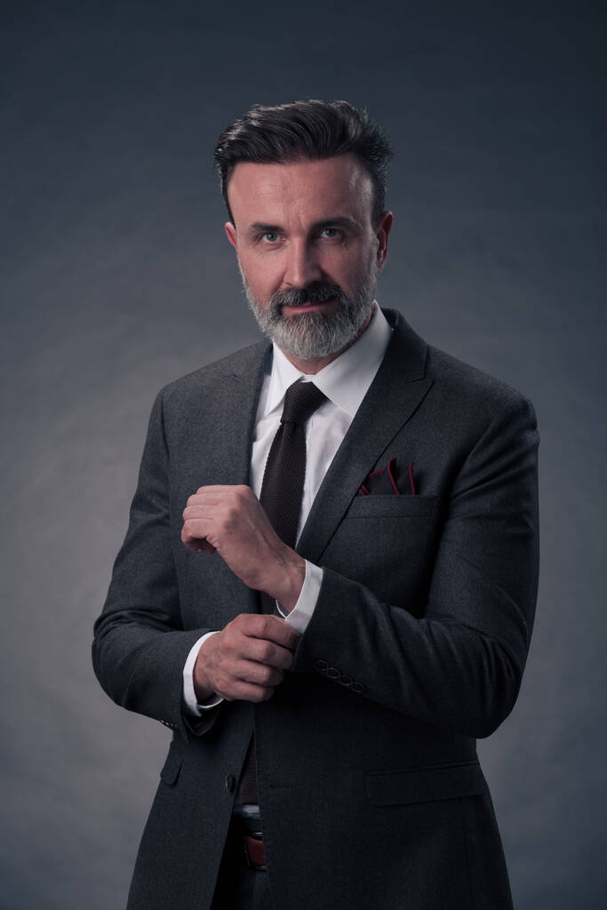 Портрет успешного стильного элегантного бизнесмена с седой бородой и повседневной деловой одеждой, уверенный в фотостудии, выделенный на темном фоне жестом руками. Качественное фото - Фото, изображение