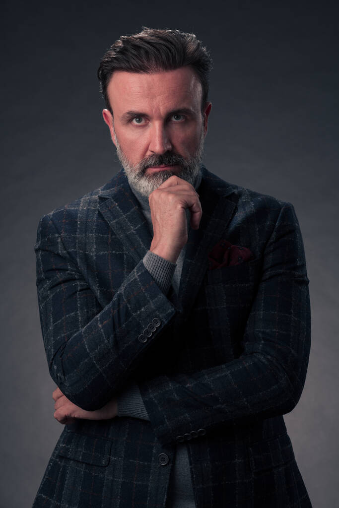 Портрет успешного стильного элегантного бизнесмена с седой бородой и повседневной деловой одеждой, уверенный в фотостудии, выделенный на темном фоне жестом руками. Качественное фото - Фото, изображение