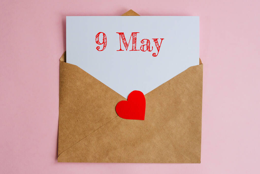 Kraft envelope with a white sheet of paper and a date 9 may, with red heart. Flat lay on pink background, romance and love concept - Photo, Image