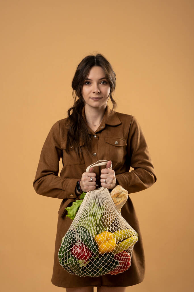 Nolla jätettä käsite. Nuori brunette nainen tilalla mesh eko laukku orgaanisia hedelmiä ja vihanneksia. Uudelleenkäytettävien virkkausverkkokassien käyttö ruokaostoksia varten. - Valokuva, kuva