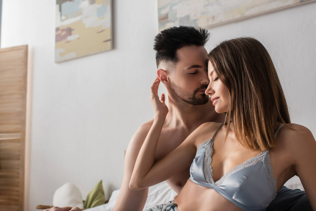 passionate woman in satin bra hugging shirtless man in bedroom - Fotografie, Obrázek