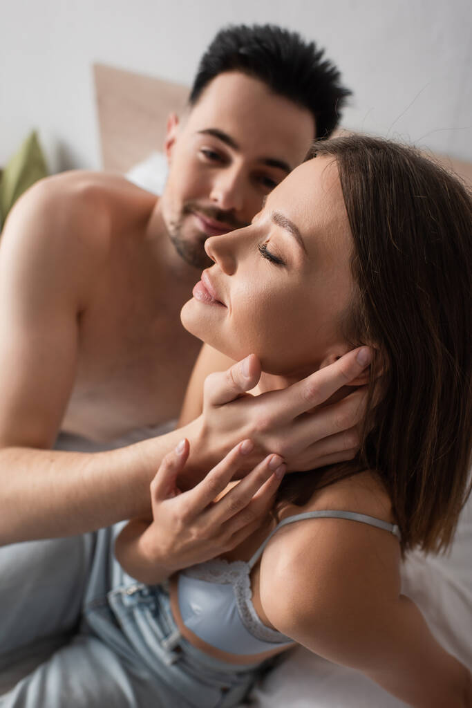 passionate woman with closed eyes near shirtless man embracing her in bedroom - Photo, image