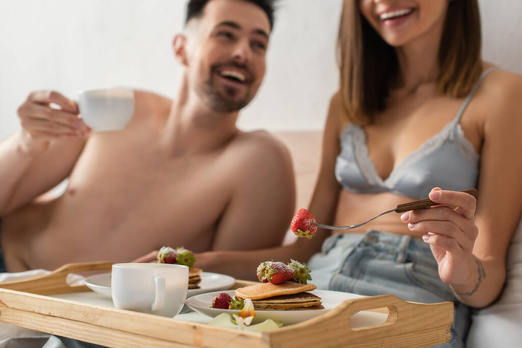 selective focus of tray with pancakes and coffee near sexy young couple smiling on blurred background - Fotoğraf, Görsel