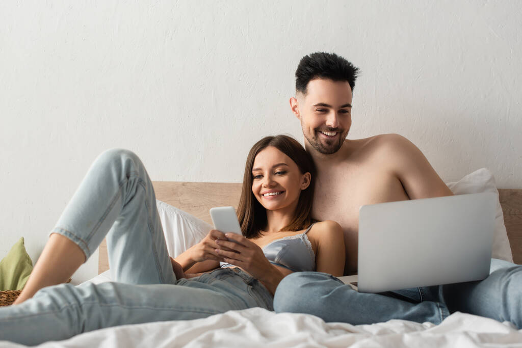 задоволена пара посміхається, використовуючи гаджети в спальні вдома
 - Фото, зображення