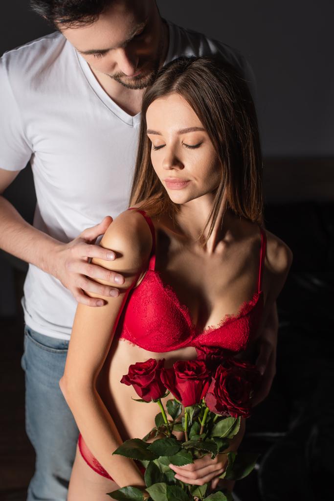 sexy woman in red bra holding bouquet of red roses near man in white t-shirt - Fotografie, Obrázek
