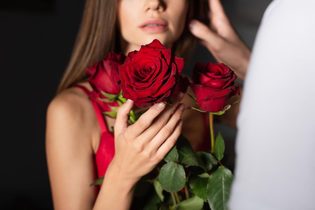 cropped view of blurred woman holding red roses near man on dark background - Φωτογραφία, εικόνα