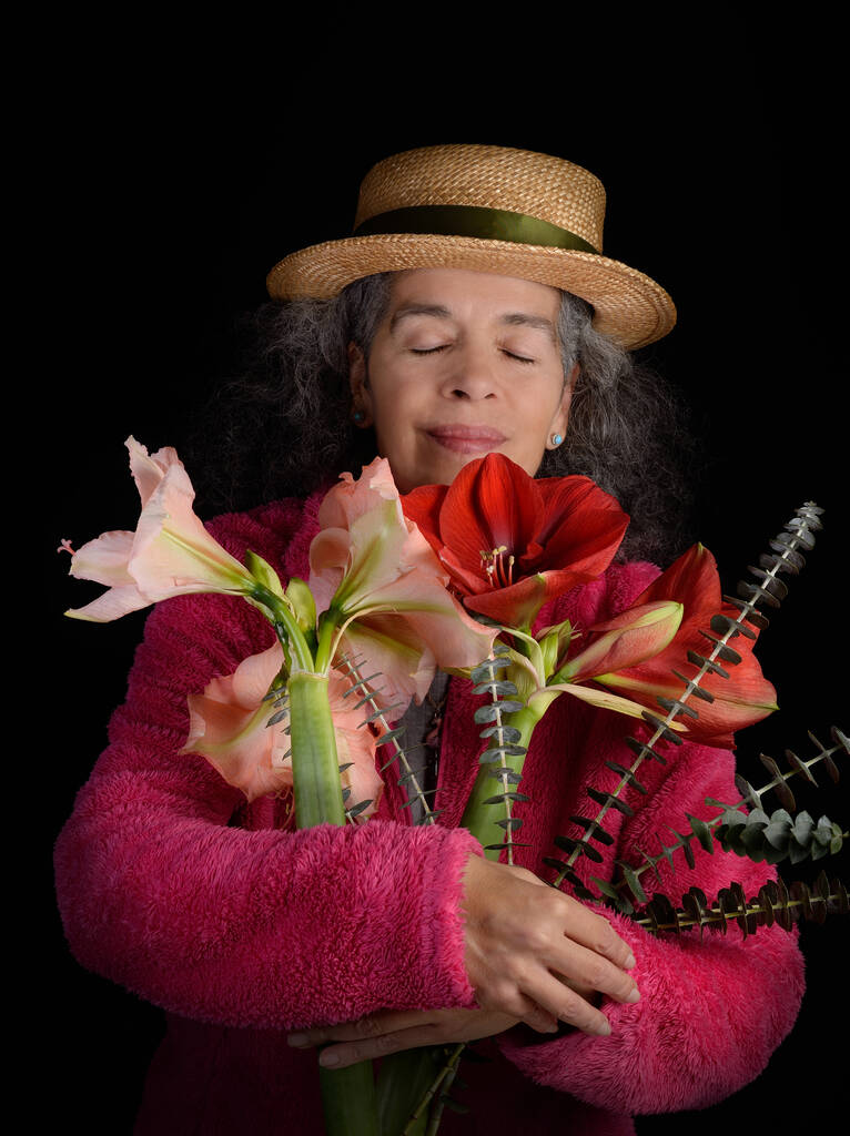 Жінка із заплющеними очима обіймає квітки Амарілліс та гілочки Евкаліптів. Темне тло. - Фото, зображення