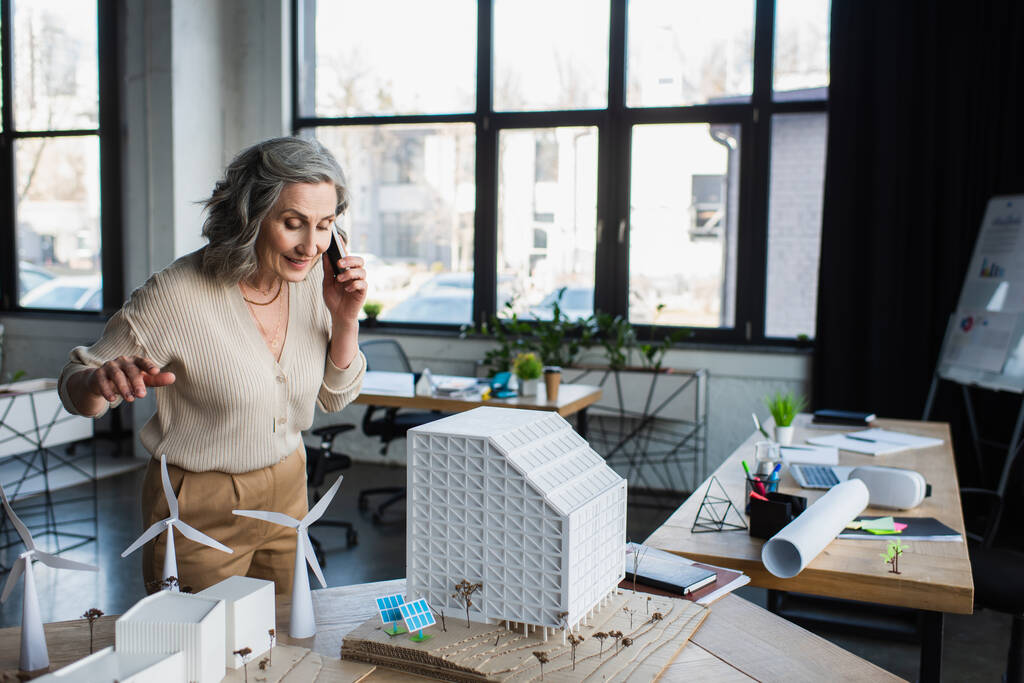 Podnikatelka mluví na smartphonu v blízkosti modelů budov a náčrtek v kanceláři  - Fotografie, Obrázek