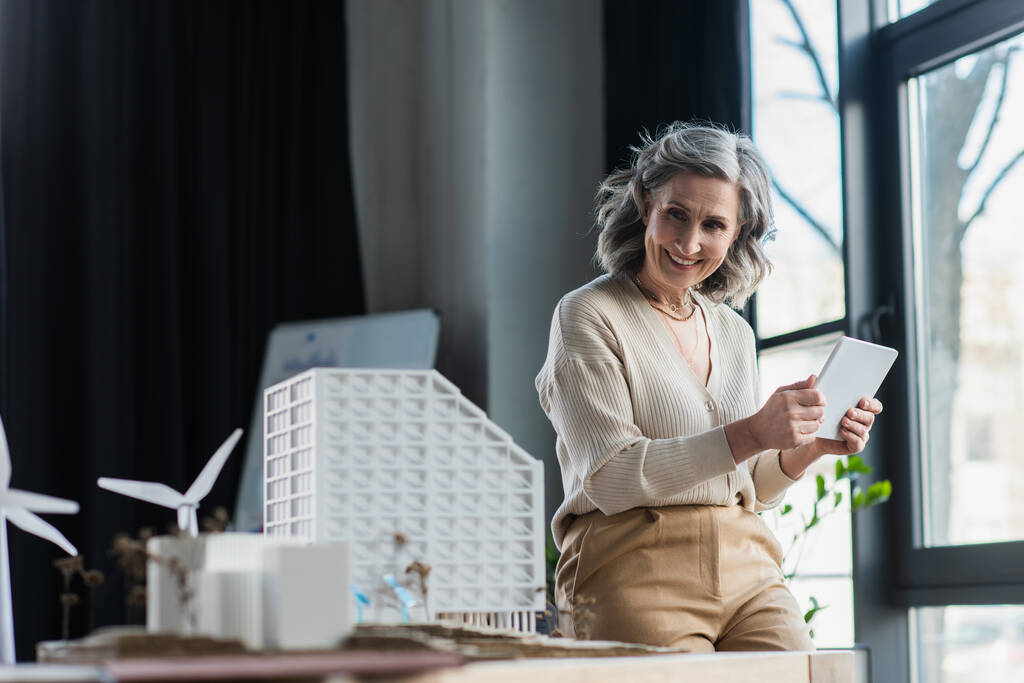 Donna d'affari che tiene tablet digitale vicino a modelli di edifici in ufficio  - Foto, immagini