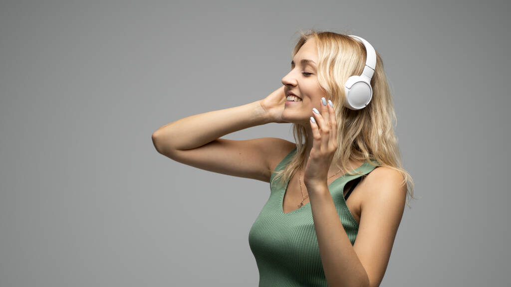 Piękna młoda kobieta słuchająca muzyki w słuchawkach na szarym tle. - Zdjęcie, obraz