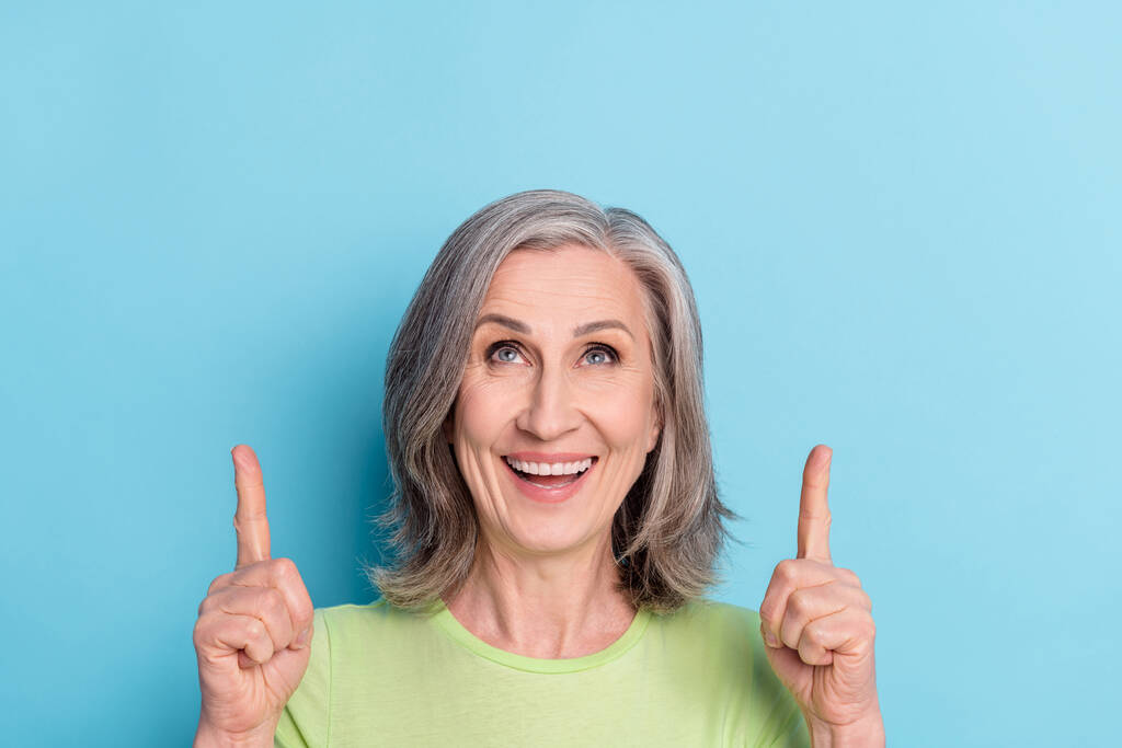 Φωτογραφία από χαρούμενα ωραία ευτυχισμένη ηλικιωμένη γυναίκα ματιά σημείο δάχτυλα κενό χώρο καλή διάθεση που απομονώνονται σε μπλε φόντο χρώμα - Φωτογραφία, εικόνα