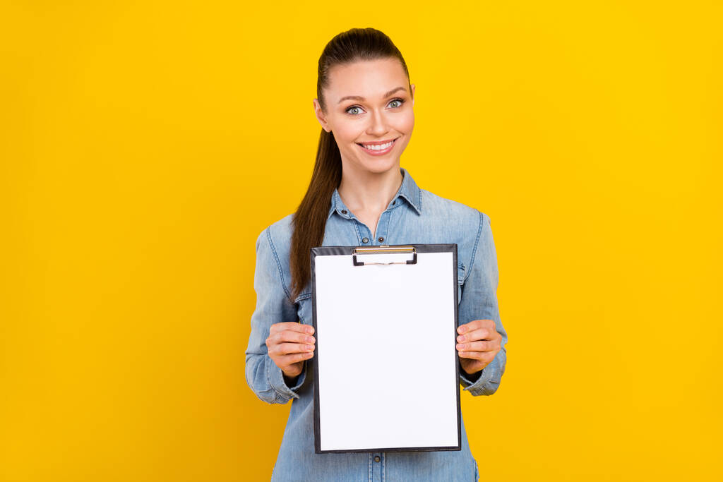 Foto retrato mujer mostrando portapapeles con espacio vacío sonriendo aislado vívido color amarillo fondo copyspace - Foto, Imagen