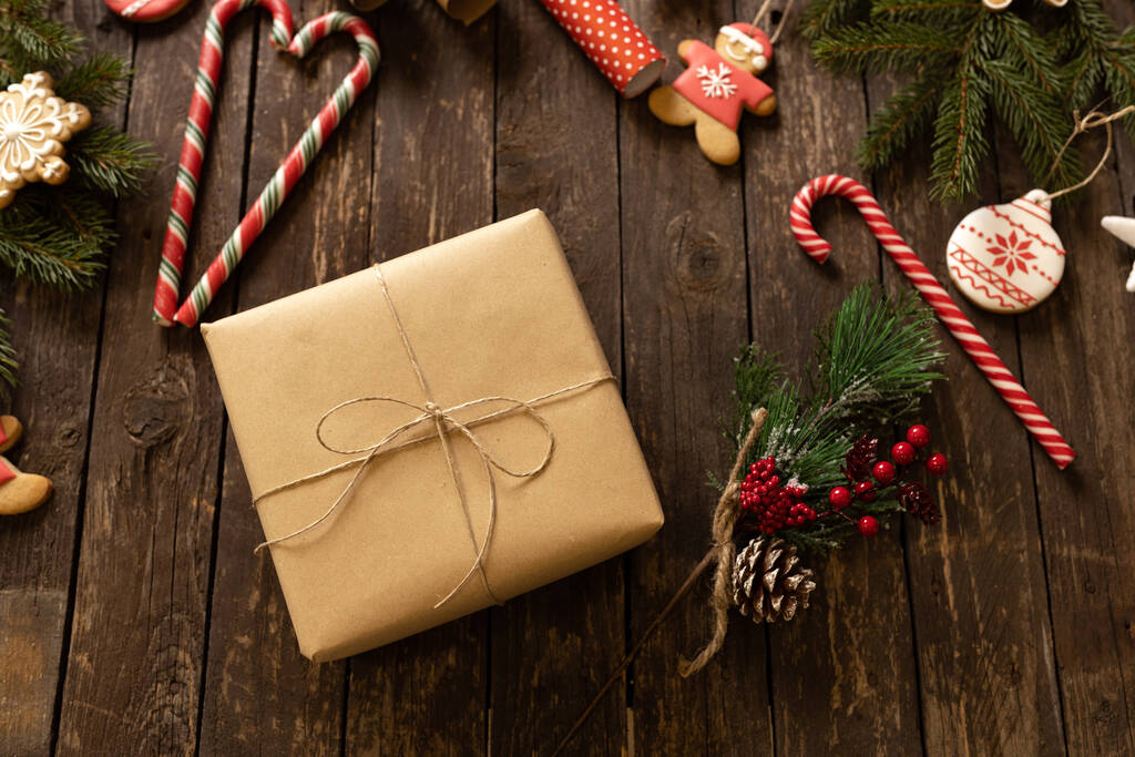 クリスマスプレゼントは、休日の装飾と木製のテーブルの上に置かれたエコペーパーに包まれ、キャンディーの杖とクリスマスクッキー、幸せな休日のコンセプト - 写真・画像