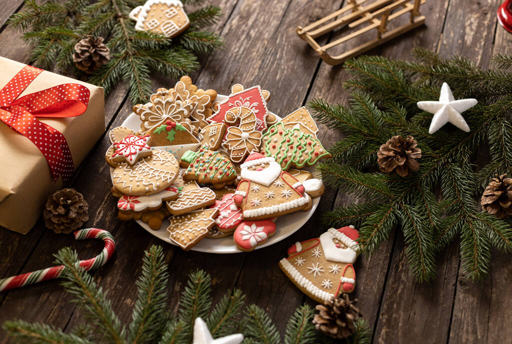 Pieczone ciasteczka świąteczne obok zapakowanego prezentu umieszczonego na drewnianym stole tła i wiecznie zielonych gałęziach, koncepcja wakacji - Zdjęcie, obraz