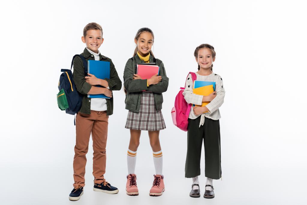joyeux écolier et écolières debout avec des sacs à dos et des cahiers sur blanc  - Photo, image