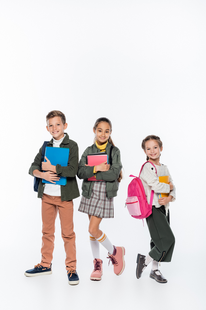 plná délka pozitivní školák a školačky stojící s batohy a notebooky na bílém  - Fotografie, Obrázek