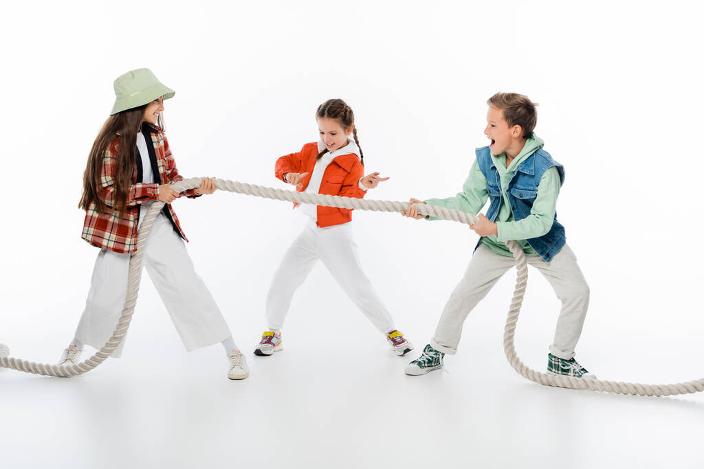 nastolatek dziecko gestykulując w pobliżu przyjaciół ciągnąc linę podczas gry holownik wojny na białym - Zdjęcie, obraz