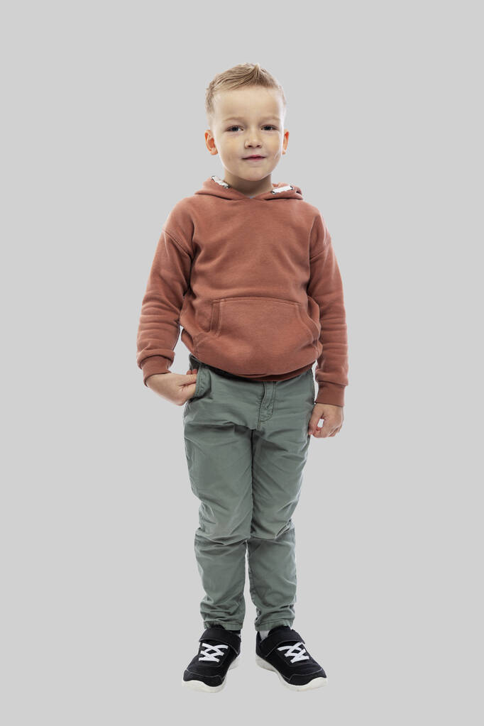 Le garçon a 5 ans. Un enfant en jean et un pull marron. Isolé sur un fond gris clair. Pleine hauteur. Vertical. - Photo, image