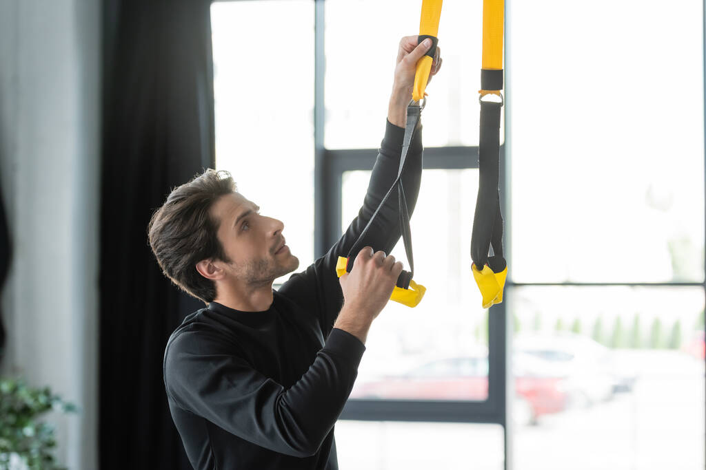 Брюнетка спортсмен регулируя ремни подвески в тренажерном зале  - Фото, изображение