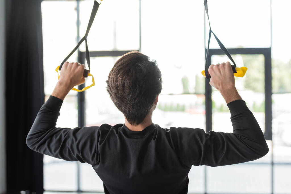 Вид сзади брюнетка спортсмен дергая ремни подвески во время тренировки в тренажерном зале - Фото, изображение