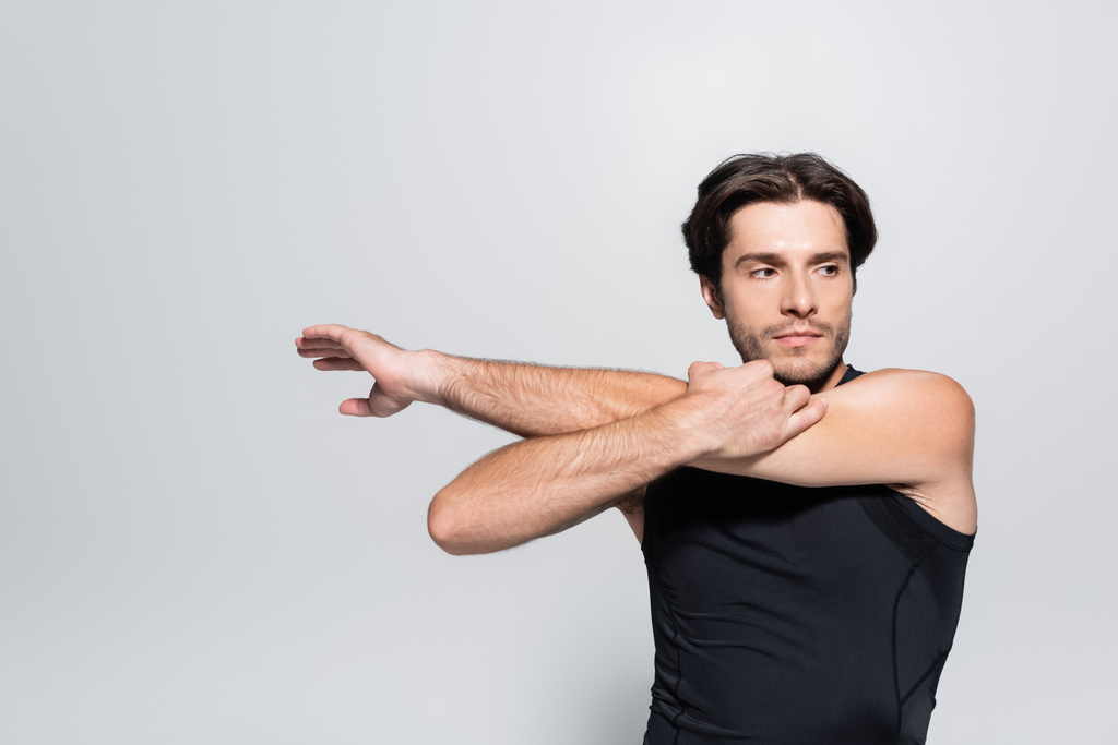 Brunette sportsman stretching arms isolated on grey  - Photo, Image