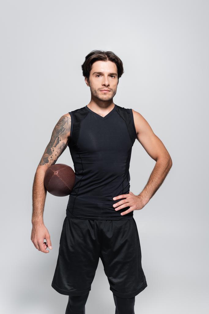 Tattooed sportsman with rugby ball looking at camera isolated on grey  - Photo, Image