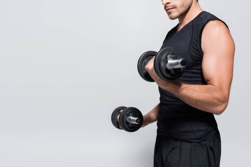 Vista recortada del deportista atlético haciendo ejercicio con pesas aisladas en gris  - Foto, Imagen