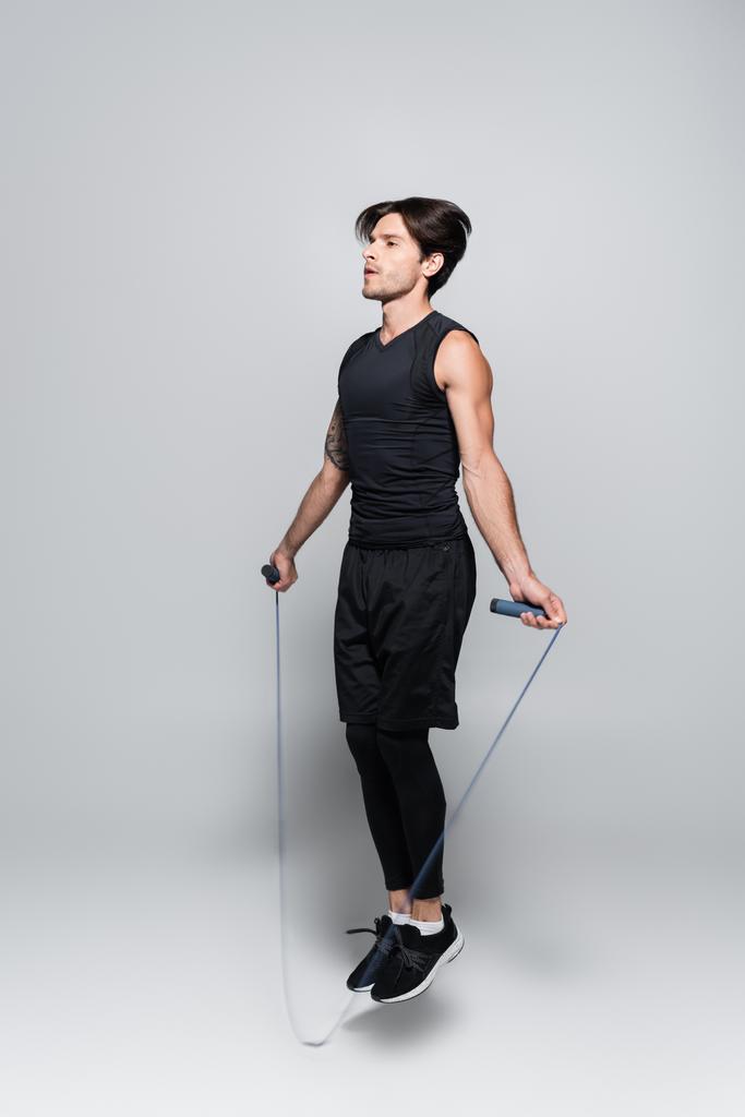 Fit Sportler Springen mit Seil auf grauem Hintergrund  - Foto, Bild
