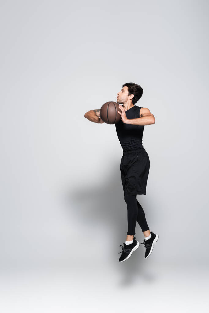 Side view of basketball player with ball jumping on grey background  - Photo, Image
