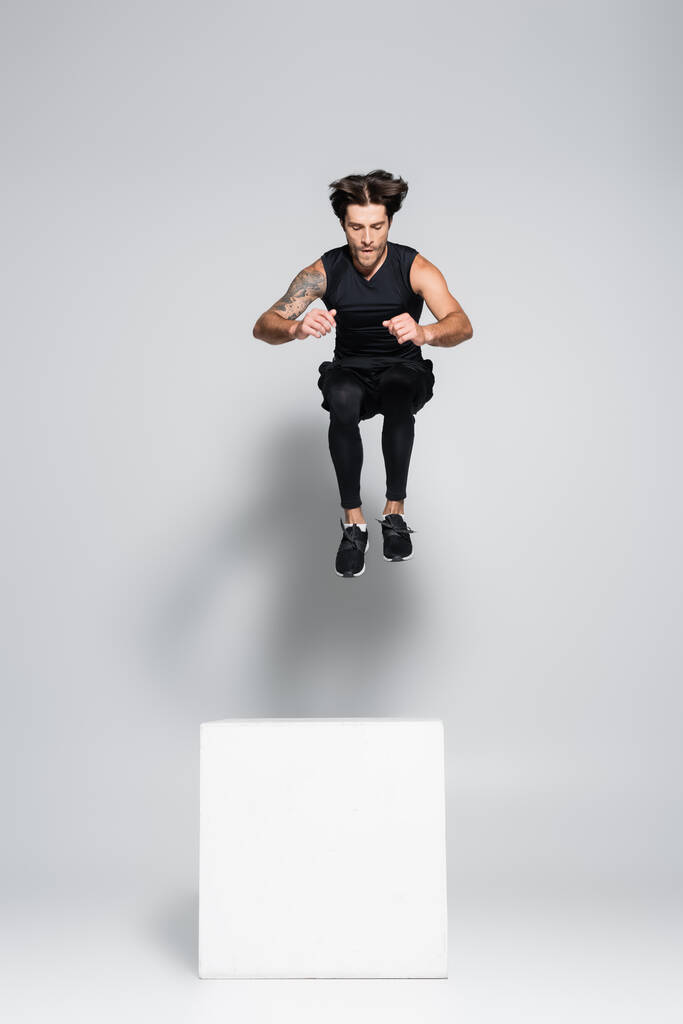 Atlétikai sportoló ugrás kocka felett szürke háttér  - Fotó, kép