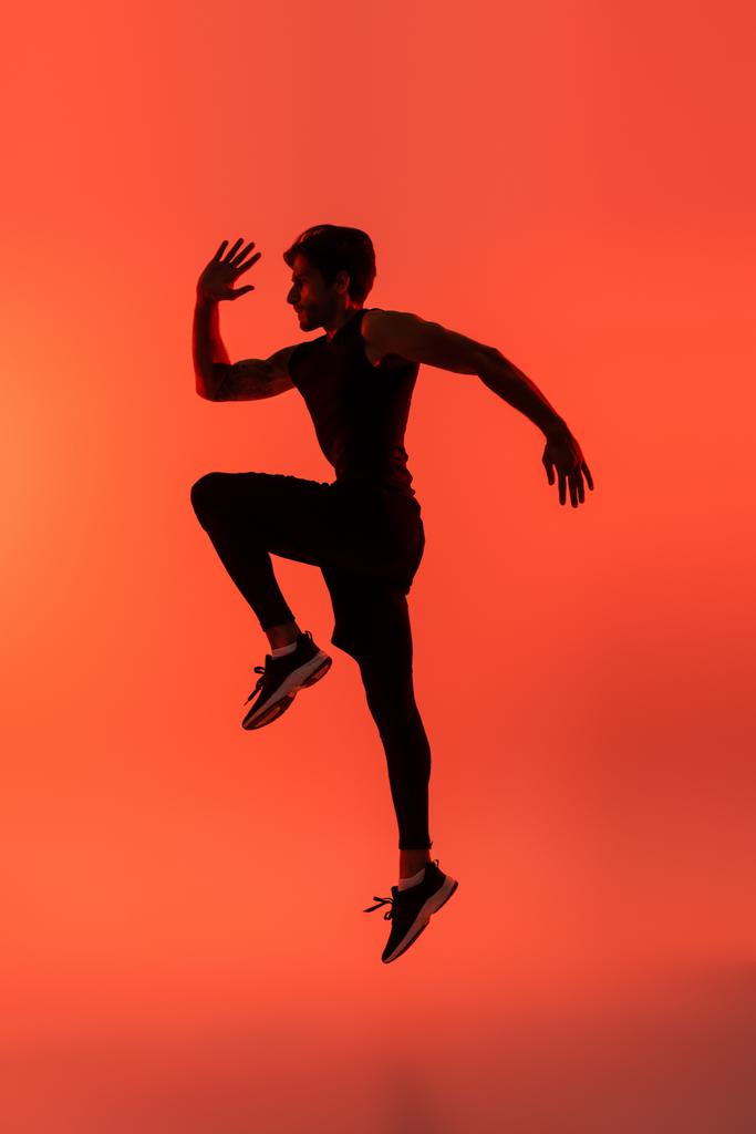 Zijaanzicht van sporter springen op rode achtergrond  - Foto, afbeelding